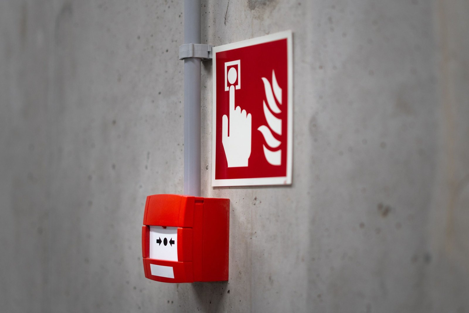Red fire alarm button and sign on a concrete wall for emergency safety indoors.